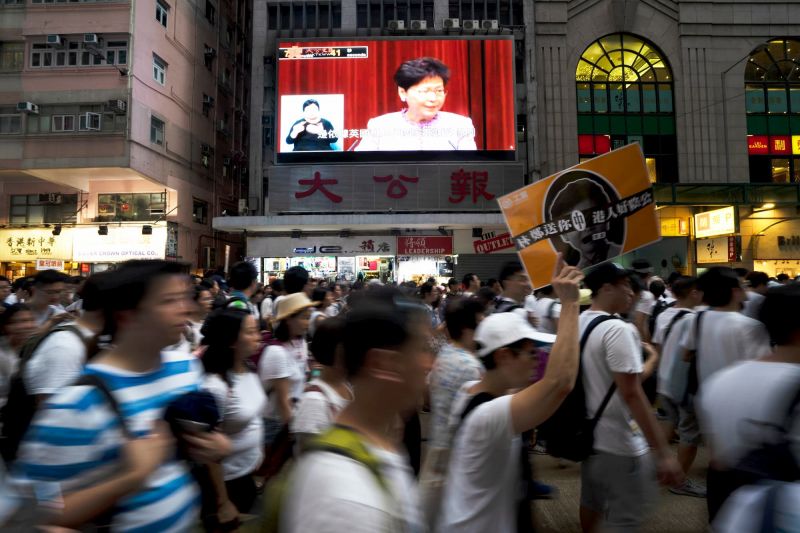 Carrie Lam appears on screen behind protesters